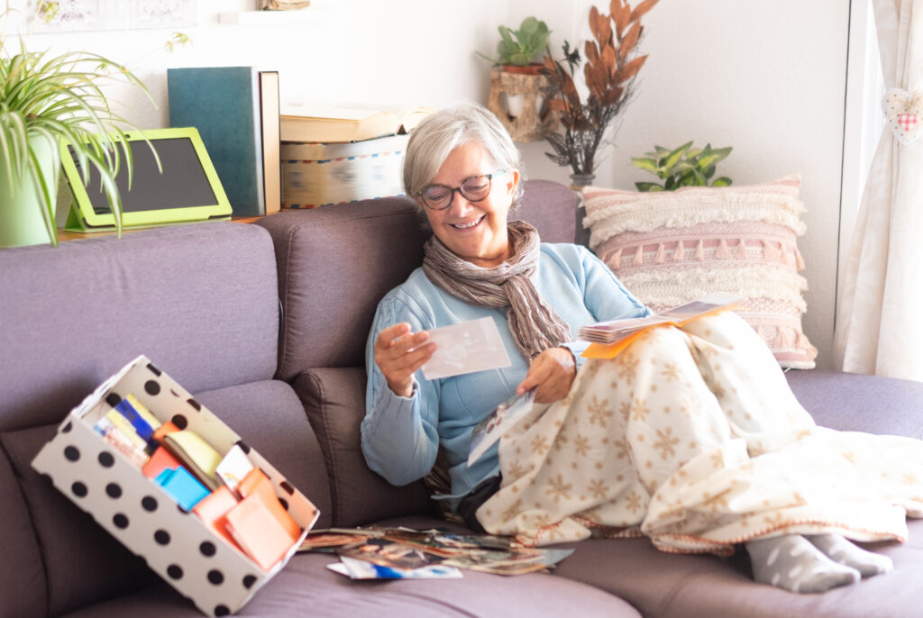 One old woman with gray hair, remembers the past looking at old photographs of a lifetime. Old mold storage. Sitting on the sofa with a mobile phone and tablet.